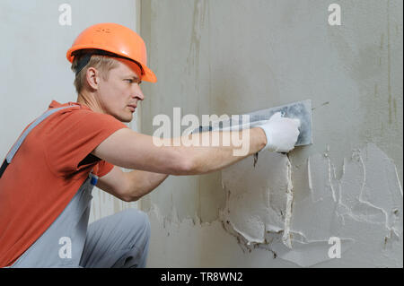 Lavoratore è mettere un gesso su una parete. Egli è con una cazzuola a lungo. Foto Stock