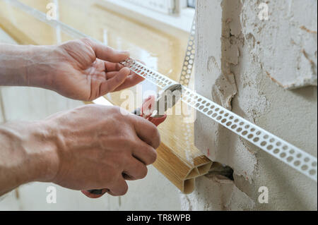 Lavoratore con le mani in mano sono il taglio di un alluminio perforato angolo per installazione su un esterno l'angolo. Foto Stock