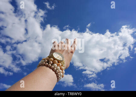 Donna di mano cercando di toccare il cielo blu che indossa bracciali e guardare Foto Stock