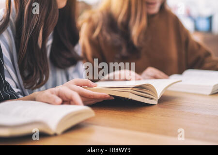 Un gruppo di giovani seduti e ci è piaciuta molto la lettura di libri insieme sul tavolo di legno Foto Stock