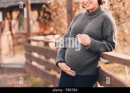 Sorridente donna incinta indossa Confortevole felpa lavorata a maglia holding pancia all'esterno. La maternità. La maternità. La felicità. Foto Stock