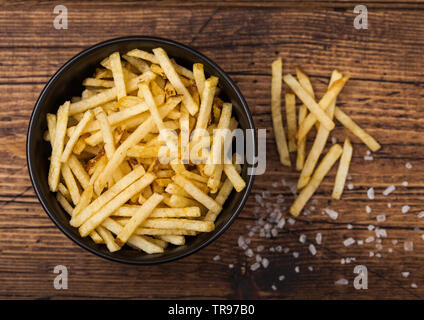 Sale e aceto bastoncini di patate in bianco ciotola, classico snack in legno. Vista superiore Foto Stock