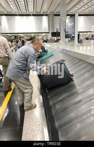 Bagagli nastro trasportatore con valigie personali muoversi in cerchio. Multirazziale persone in attesa per i loro bagagli. L'Aeroporto Internazionale di Hong Kong. Foto Stock