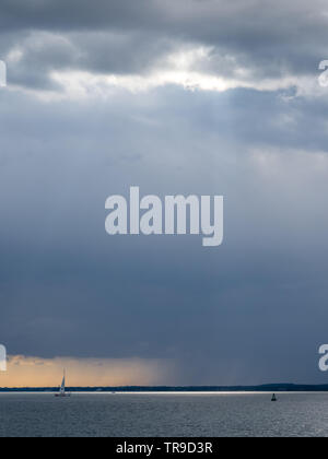 Un movimento rainfront avvicinando oltre Solent con lone singolo yacht a vela in mare con la boa sotto big sky nuvole temporalesche arancione tramonto Foto Stock