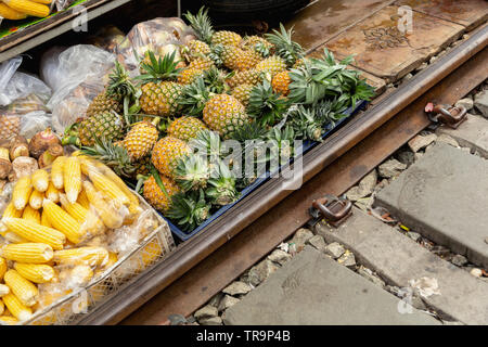 L'ananas e il mais in vendita lungo le piste al Maeklong mercato ferroviario, Bangkok, Thailandia Foto Stock