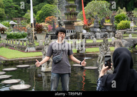 Yong donna indonesiana il hijab come scattare una foto del suo ragazzo in acqua Palace di Tirta Gangga, Karangasem, Bali, Indonesia. Locali di turisti indonesiani Foto Stock