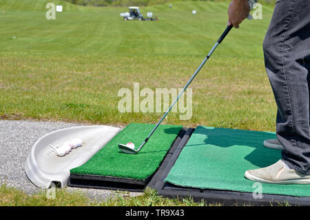 Il golfer imposta la sua pratica tiro su un driving range. Sullo sfondo il trattore utilizzato per raccogliere le sfere fuori dal terreno. Foto Stock
