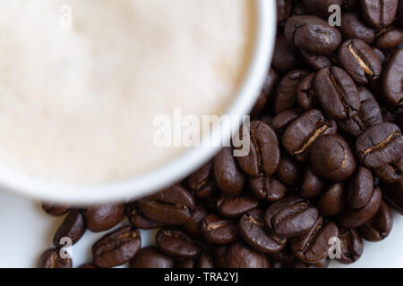 Materie semi caffè sul piatto bianco e bianco sfocata tazza di caffè caldo sul lato, Foto Stock