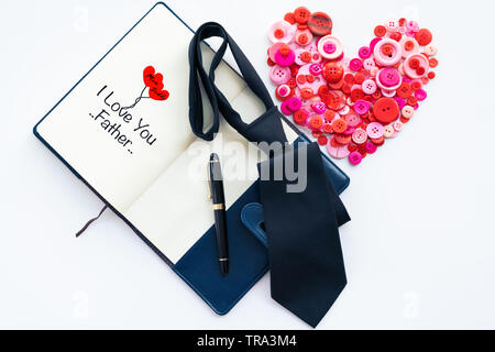 I padri felice giorno, pulsante rosso a forma di cuore e cravatta scuro sul libro e la penna di lusso con il testo ti amo padre Foto Stock