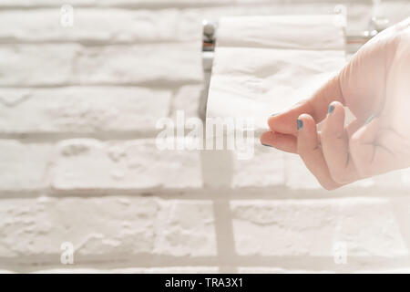 Femmina tirando a mano una carta velina bianca dal rotolo di tessuto nella toilette. Foto Stock