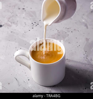 Versa il latte in una tazza da bianco creamer tè su un grigio Sfondo tessiturali Foto Stock