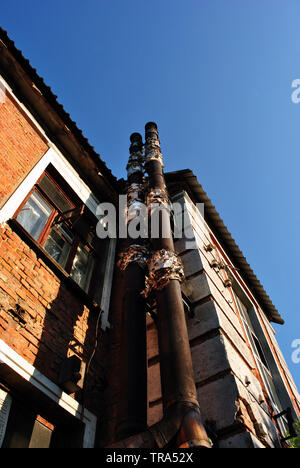 Muro di mattoni di edificio con tubi vecchi, vista dall'alto sul tetto in ardesia e cielo blu Foto Stock