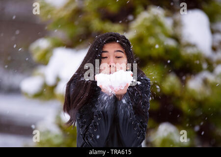 Biracial teen ragazza in piedi all'aperto in inverno neve fuori mano, con coperta di neve verde di pini in background Foto Stock