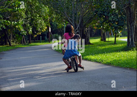 Carino il colpo di due ragazze seduti insieme su una bicicletta escursioni in bicicletta nel parco del sole estivo Foto Stock