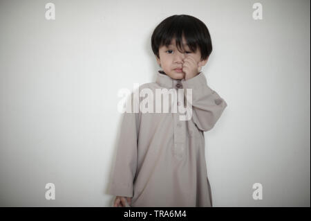 Ritratto di un giovane musulmano asiatici Ragazzo che guarda stanco e deluso durante Hari Raya celebrazione in casa Foto Stock