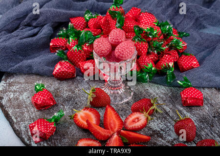 Caramelle alla fragola e al gusto di fragola il concetto di caramelle con vicino sul dolce e aspro rosso cinghie acide ricoperta di zucchero isolato su una tavola di legno backgrou Foto Stock