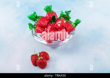 Caramelle alla fragola e al gusto di fragola il concetto di caramelle con vicino sul dolce e aspro rosso cinghie acide ricoperta di zucchero isolato su una tavola di legno backgrou Foto Stock