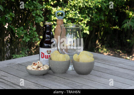 Sint Gillis waas, Belgio - 22 luglio 2018 Duvel Belgio birra su di una terrazza giardino con il formaggio feta e patatine salate e un di legno apribottiglie Foto Stock