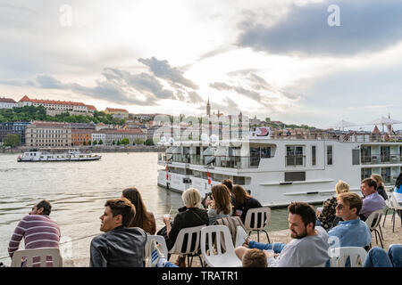 Persone sedute e socializzare con un drink al bar estivo sulla riva del Danubio vicino ad un famoso Ponte delle catene sul lato Pest di Budapest, Ungheria. Foto Stock