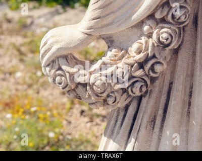 Dettaglio di una statua femminile di pietra, la sinistra vista dal lato posteriore, una donna di mano che tiene una ghirlanda di rose, lei cade leggermente al di sopra della gonna oscillante par Foto Stock