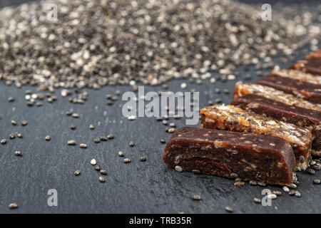 Close up di proteina energy bar con semi di chia ingrediente non focalizzato e pila di chia sullo sfondo. Paleo dieta concetto. Foto Stock