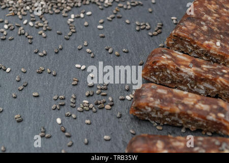 Close up di proteina energy bar con semi di chia ingrediente non focalizzato e pila di chia sullo sfondo. Paleo dieta concetto. Foto Stock