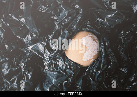 Globo di sughero che rappresenta il pianeta terra tra il nero dei sacchetti di plastica e affondamento. Ocean plastica problema di inquinamento del concetto. Foto Stock