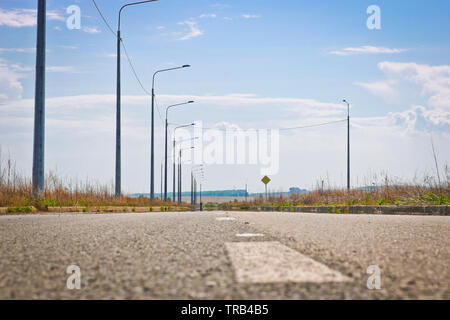 Abbandonata la strada asfaltata con indicazioni stradali e un certo numero di lampade di illuminazione sul lato della strada. Messa a fuoco selettiva Foto Stock