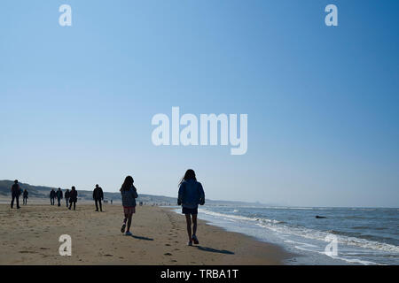 Gruppi di persone a godersi una passeggiata lungo la spiaggia in bright srping sole con mare calmo e cielo blu