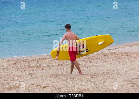RNLI Lifeguard che porta surf board in riva al mare a Bournemouth Beach, Dorset UK nel mese di giugno
