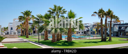 Lussureggianti palme all'interno di urbanizzazione chiusa con prato verde piscina case moderne a sunny giorno d'estate. Nuovo albergo in Spagna, nessun popolo Foto Stock