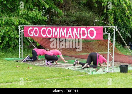 Warrington, Regno Unito. 2 Giugno 2019. Gara per la Vita 2019, Warrington, in aiuto della ricerca sul cancro. Tre donne strisciare sotto la rete di un ostacolo Foto Stock