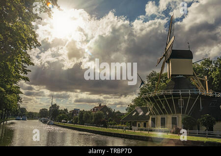 Ampia canal con mulino a vento e le barche e la lucentezza del tramonto riflesso in acqua a Weesp. Piacevole villaggio pieno di canali e verde in Paesi Bassi. Foto Stock