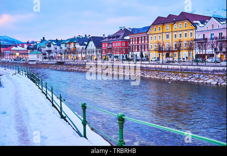 Godetevi il tramonto camminando lungo la passeggiata innevata del fiume Traun con una vista sulle colorate case tradizionali e il cielo luminoso riflesso in increspata Foto Stock