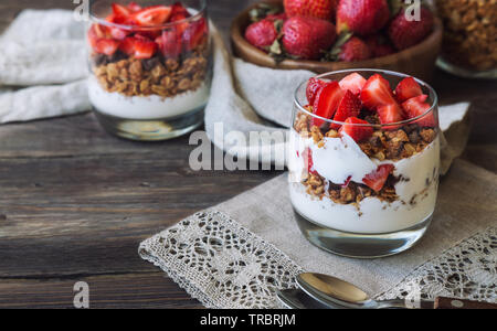 In casa granola, muesli con scaglie di cioccolato e fragole e yogurt in bicchieri in legno rustico sfondo. Una sana prima colazione. Foto Stock