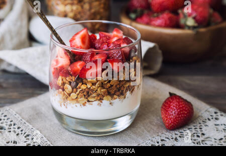 In casa granola, muesli con scaglie di cioccolato e fragole e yogurt in vetro su legno rustico sfondo. Una sana prima colazione. Foto Stock