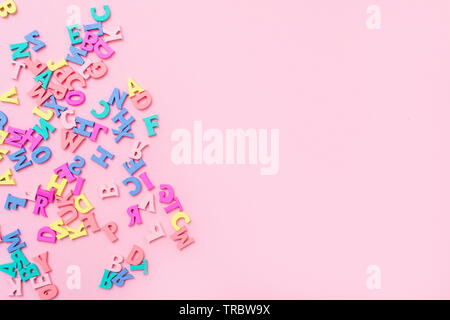 Molti variopinti lettere in legno su un sfondo rosa. toy lettere dell'alfabeto inglese. Vista da sopra. Lay piatto. Copia spazio per il testo Foto Stock