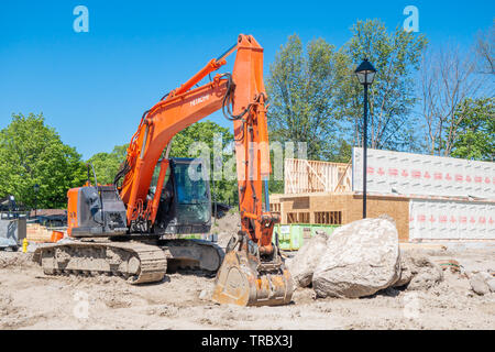 Escavatore si siede di fronte a una nuova casa in costruzione in una suddivisione di sviluppo. Foto Stock
