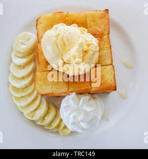 Pane dolce miele santos gelato alla vaniglia con panna montata banana di frutta e miele delle api su piastra bianca nella caffetteria cafe Foto Stock