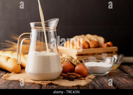 Versare il latte in un recipiente posto sul sacco. Un sacco di pane e uova giacciono su di un tavolo di legno. Foto Stock