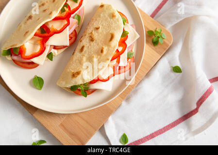 Casalingo italiano piadina con formaggio e pomodoro, prosciutto, pepe rosso e basilico su una piastra bianca su una bianca tavolo in legno. Cucina Italiana. Vista laterale, copia spa Foto Stock