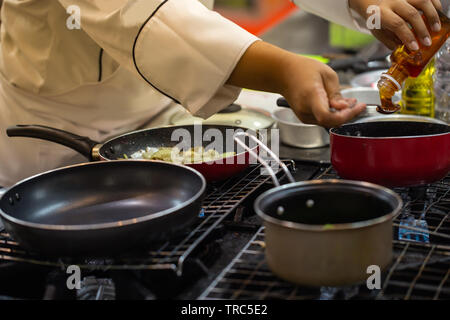 Lo Chef versando il miele di cucchiaino di salsa di cottura in casseruola Foto Stock