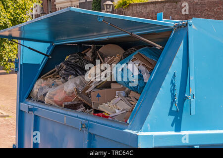 Blue contenitore di rifiuti con sportellino aperto pieno di rifiuti Foto Stock