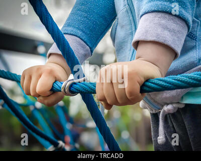 Close up del ragazzo in mani tiene la corda mentre sta salendo sulla corda climbing net a scuola parco giochi. Foto Stock