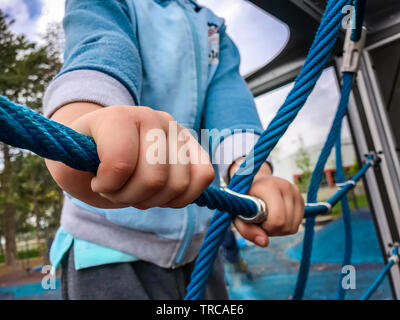 Close up del ragazzo in mani tiene la corda mentre sta salendo sulla corda climbing net a scuola parco giochi. Foto Stock