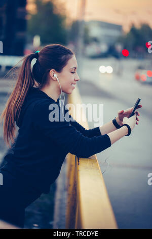 Sporty giovane donna utilizzando un telefono cellulare mentre si lavora fuori sul ponte Foto Stock