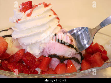 Closeup cucchiaio scooping nel gelato alla fragola e rabboccato con frutti di bosco freschi e panna montata Foto Stock