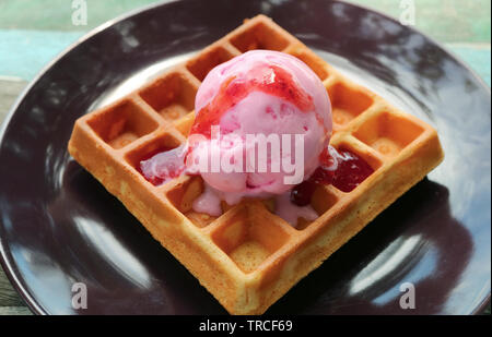Freschi di forno Waffle guarnita con gelato alla fragola sul marrone scuro piastra Foto Stock