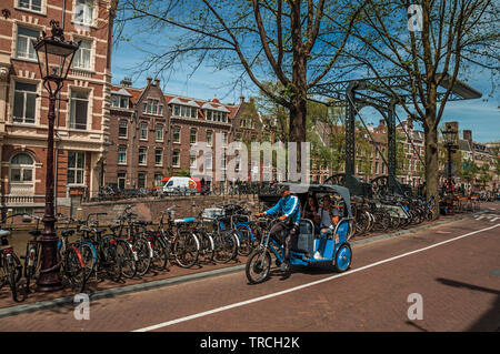 In rickshaw equitazione sulla strada accanto al canale e vecchi edifici a Amsterdam. Città con enorme attività culturali, dei canali e dei ponti nei Paesi Bassi. Foto Stock