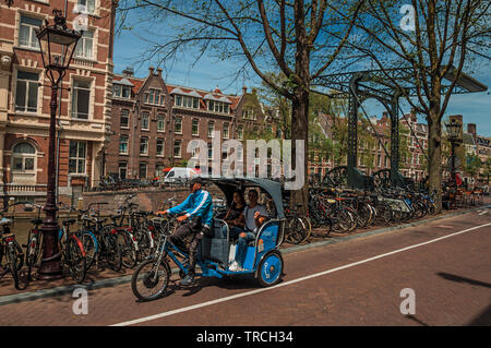 In rickshaw equitazione sulla strada accanto al canale e vecchi edifici a Amsterdam. Città con enorme attività culturali, dei canali e dei ponti nei Paesi Bassi. Foto Stock